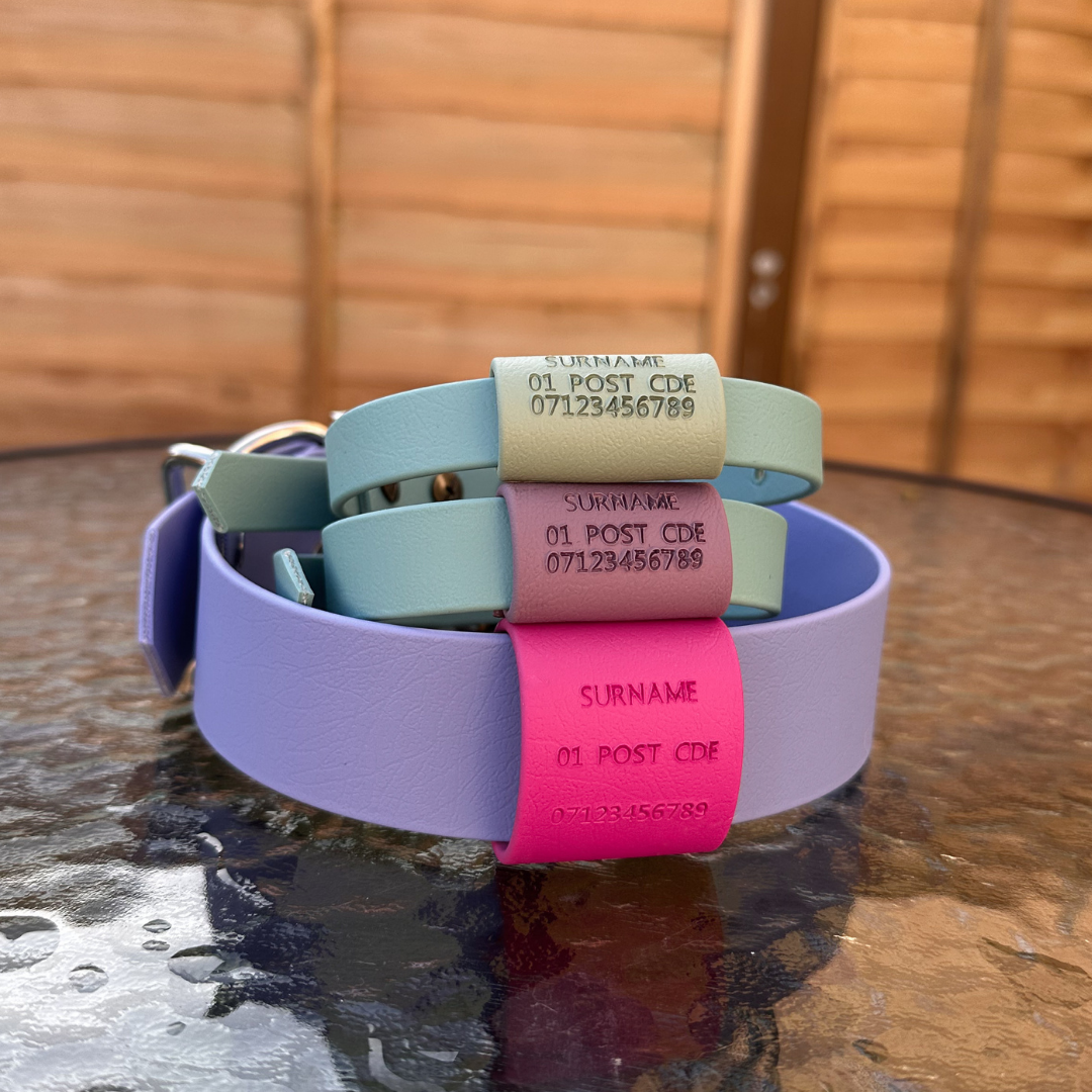 A selection of custom Biothane slide on dog tags in various colours, each with personalised text including a surname and a phone number and address 